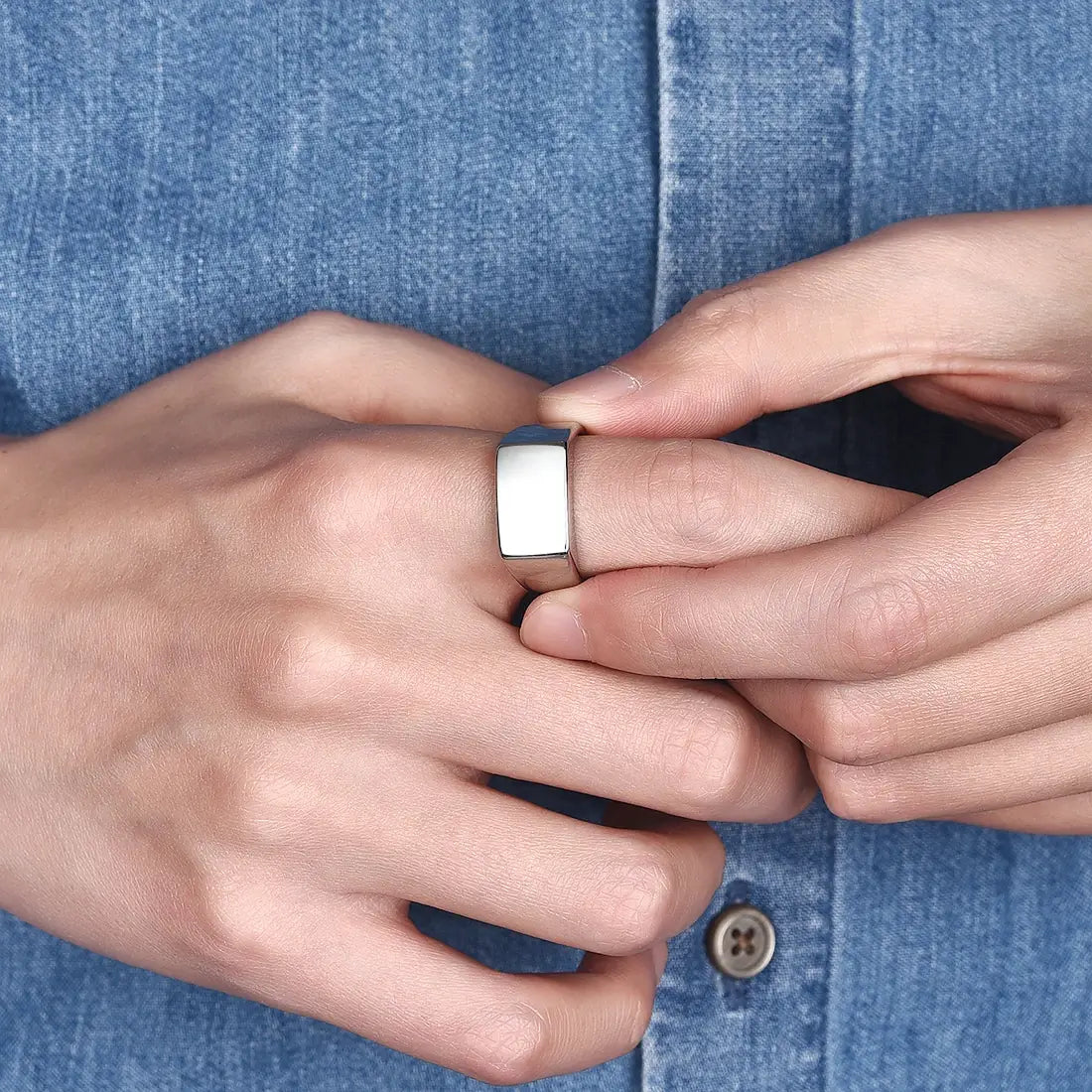 Bague chevalière en acier plaqué or blanc portée au doigt d'un homme.