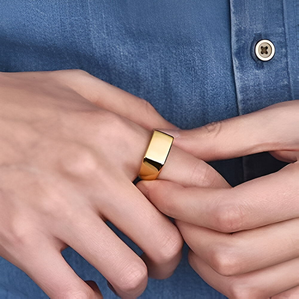 Bague chevalière en acier plaqué or jaune portée au doigt d'un homme.