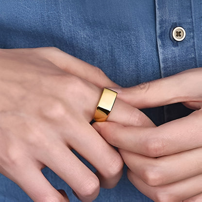 Bague chevalière en acier plaqué or jaune portée au doigt d'un homme.