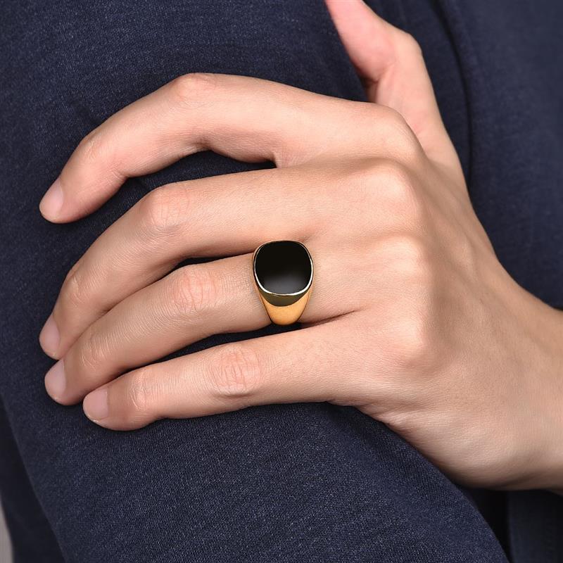 Bague chevalière en acier et or jaune sertie d'onyx portée au doigt d'un homme.