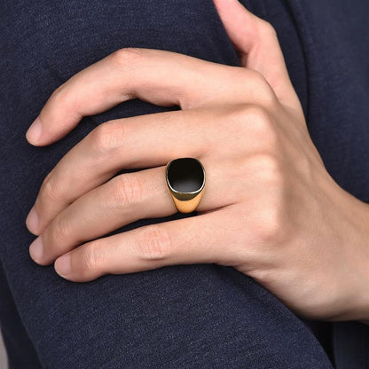 Bague chevalière en acier et or jaune sertie d'onyx portée au doigt d'un homme.