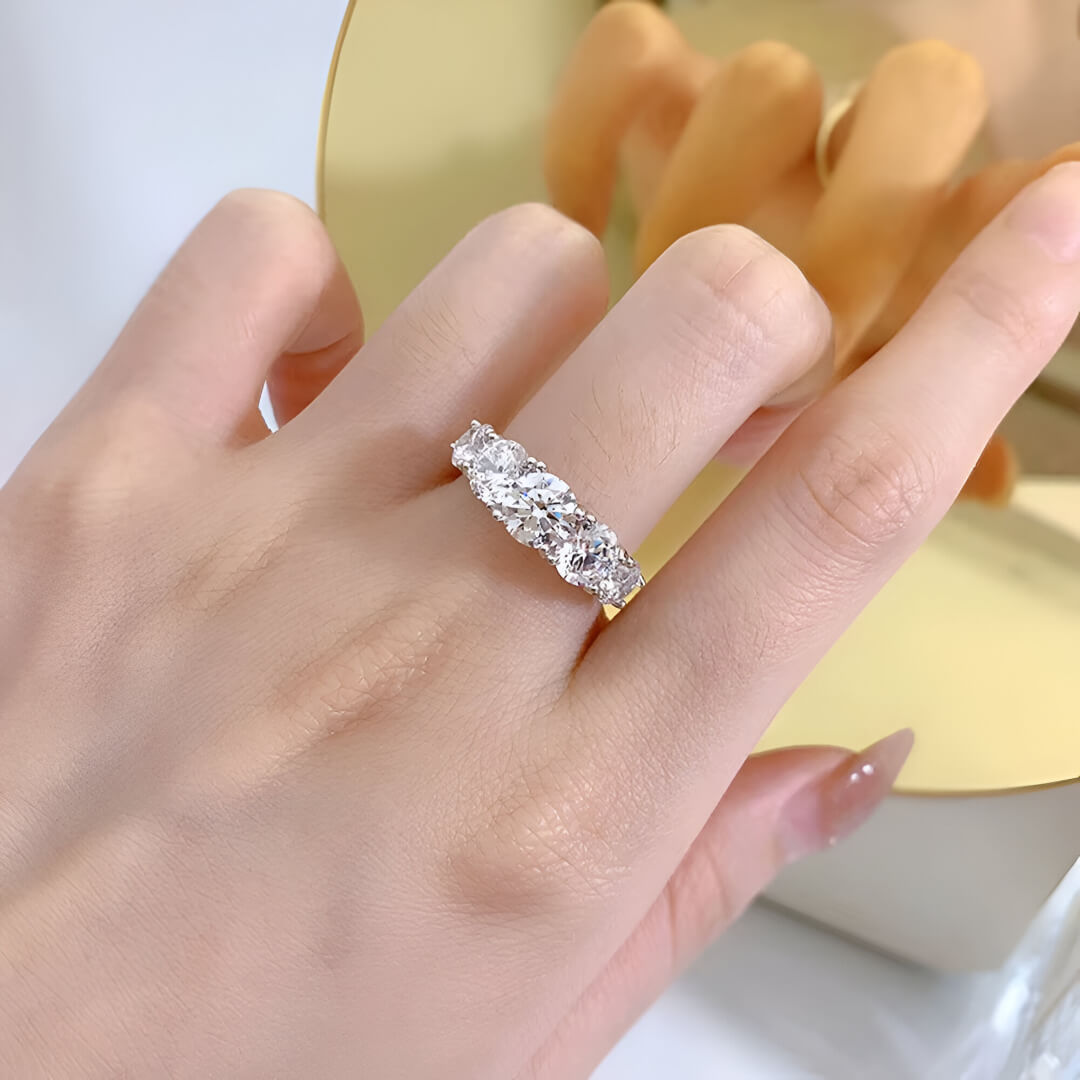 Bague de fiançailles cinq pierres en or blanc et diamants synthétiques portée au doigt d'une femme vue du dessus.