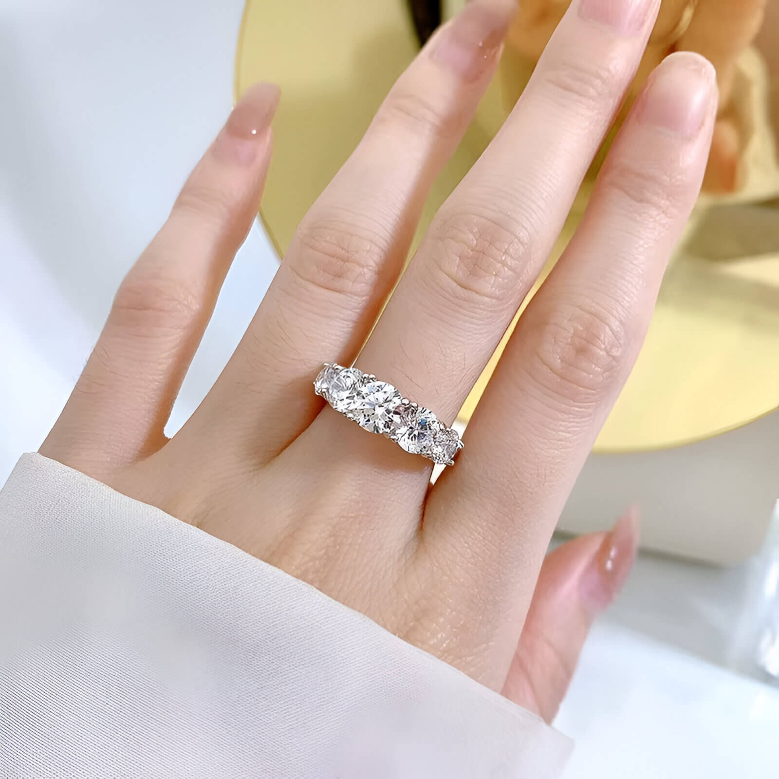 Bague de fiançailles cinq pierres en or blanc et diamants synthétiques portée au doigt d'une femme.