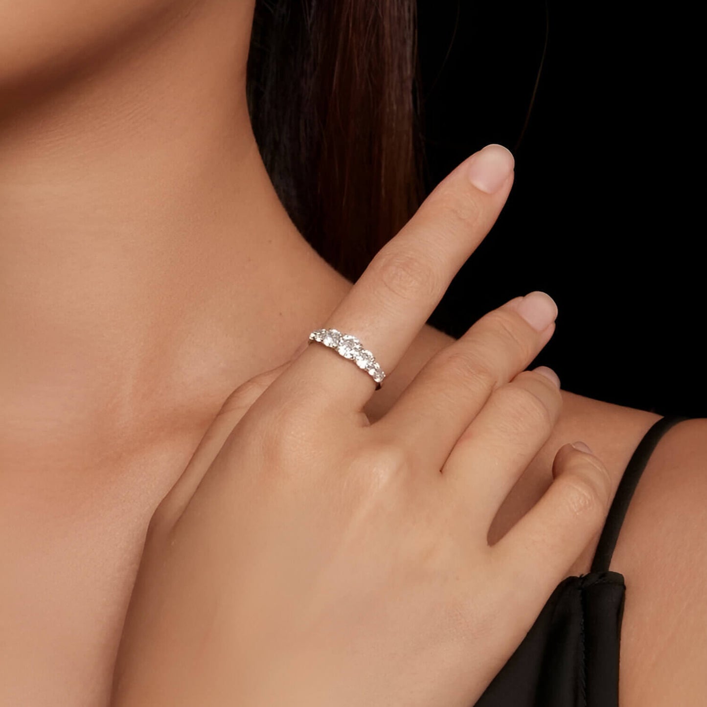 Bague cinq pierres graduées en or blanc et diamants synthétiques portée au doigt d'une femme vue de loin.