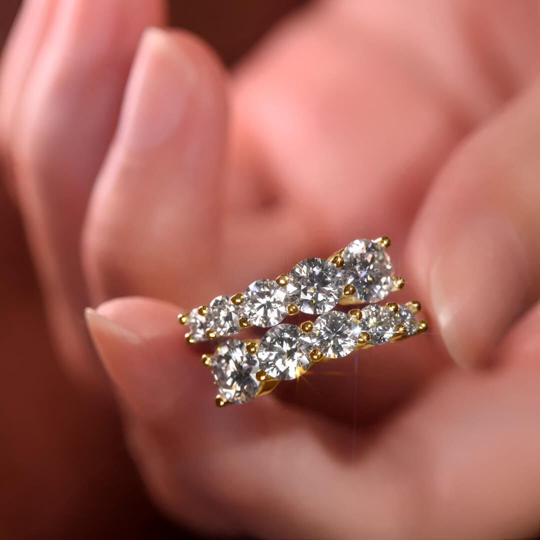 Bague de fiançailles dix pierres en argent sterling 925 plaqué or jaune et diamants montrée entre les doigts d'une femme vue de face.