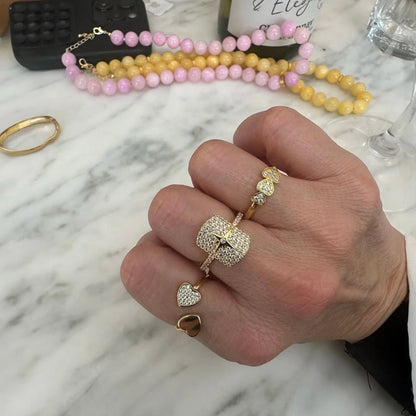 Bague double cœur doré Lumira en acier plaqué or jaune 18K raffiné et petits diamants ronds portée au doigt d'une femme vue du dessus.