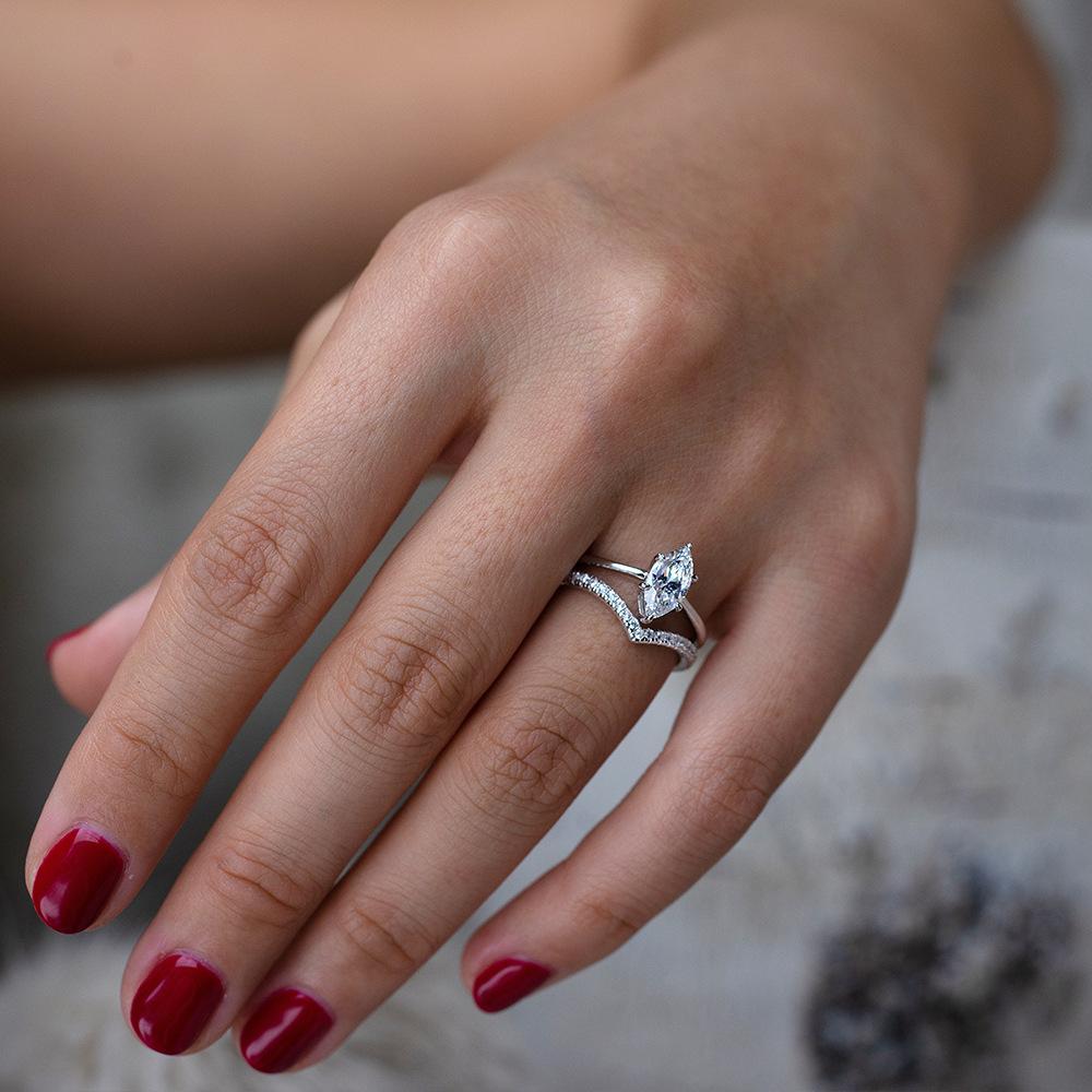 Bague duo de fiançailles en or blanc et diamants synthétiques portée au doigt d'une femme.