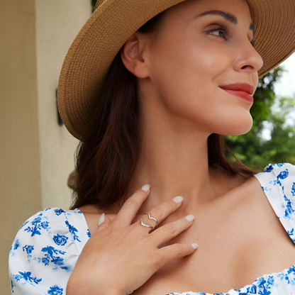 Bague fantaisie ouverte en or blanc portée au doigt d'une femme vue de loin.