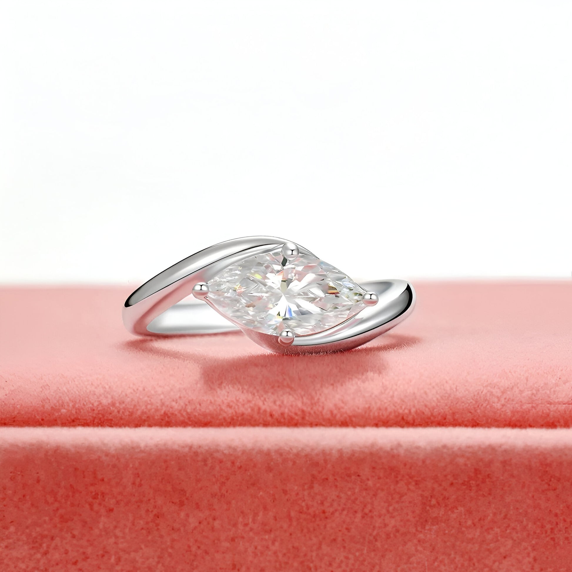 Bague diamant marquis solitaire à plat vue de face sur une surface rose bonbon.