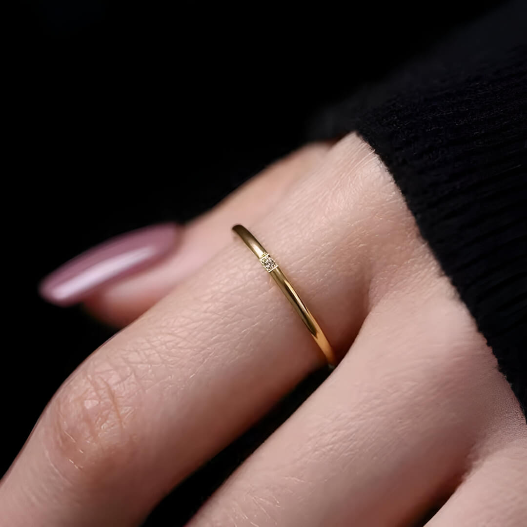 Variante 1 pierre de la bague fine 1mm Cassiane en acier inoxydable plaqué or jaune 18K et oxyde de zirconium portée au doigt d'une femme vue de proche.