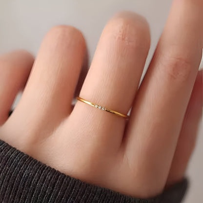 Variante 3 pierres de la bague fine 1mm Cassiane en acier 316L plaqué or jaune 18K et oxyde de zirconium portée au doigt d'une femme vue de proche.