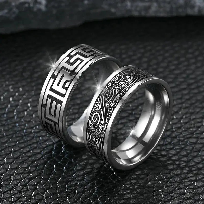 Bague gravée à bande en acier blanc variantes géométrique et fluide debout sur fond noir.