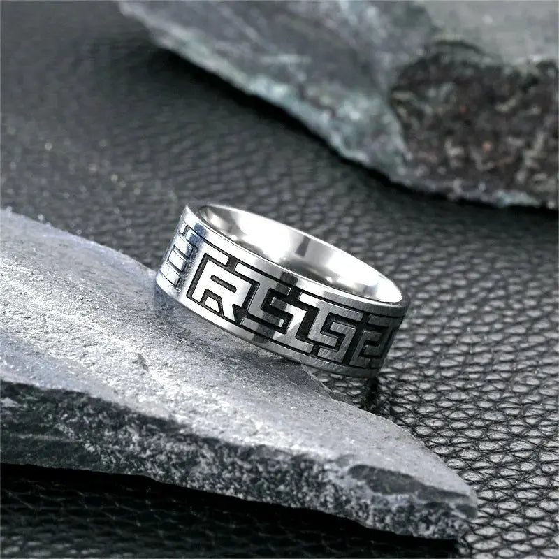 Bague gravée à bande en acier blanc variante géométrique posée sur une pierre.