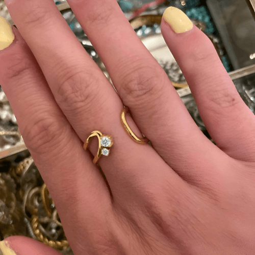 Bague ouverte courbée en acier et or jaune sertie d'oxydes de zirconium portée au doigt d'une femme.