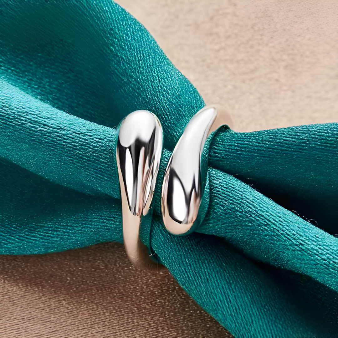 Bague ouverte en argent goutte d'eau portée sur une nappe bleue cyan, vue d'ensemble qui montre son design moderne et raffiné. Le plaquage or blanc 14K apporte une touche de luxe et de sophistication - La Petite Rebelle