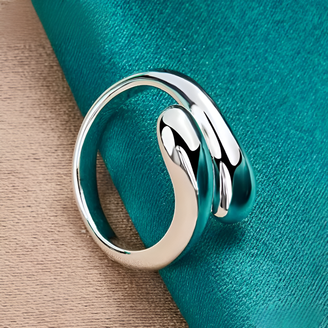 Vue rapprochée de la bague ouverte en argent goutte d'eau sur nappe bleue cyan. Un bijou délicat et moderne qui se distingue par son design contemporain et son plaquage or blanc 14K - La Petite Rebelle