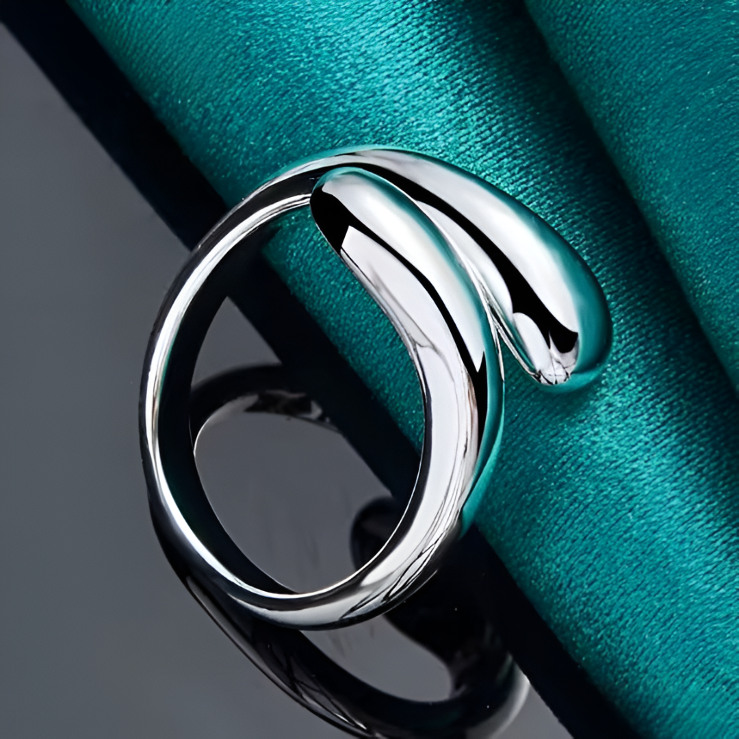 Bague ouverte en argent goutte d'eau posée délicatement sur une nappe bleue cyan, un accessoire chic au design soigné qui capture la lumière, réalisé avec un alliage de zinc et plaqué or blanc 14K - La Petite Rebelle