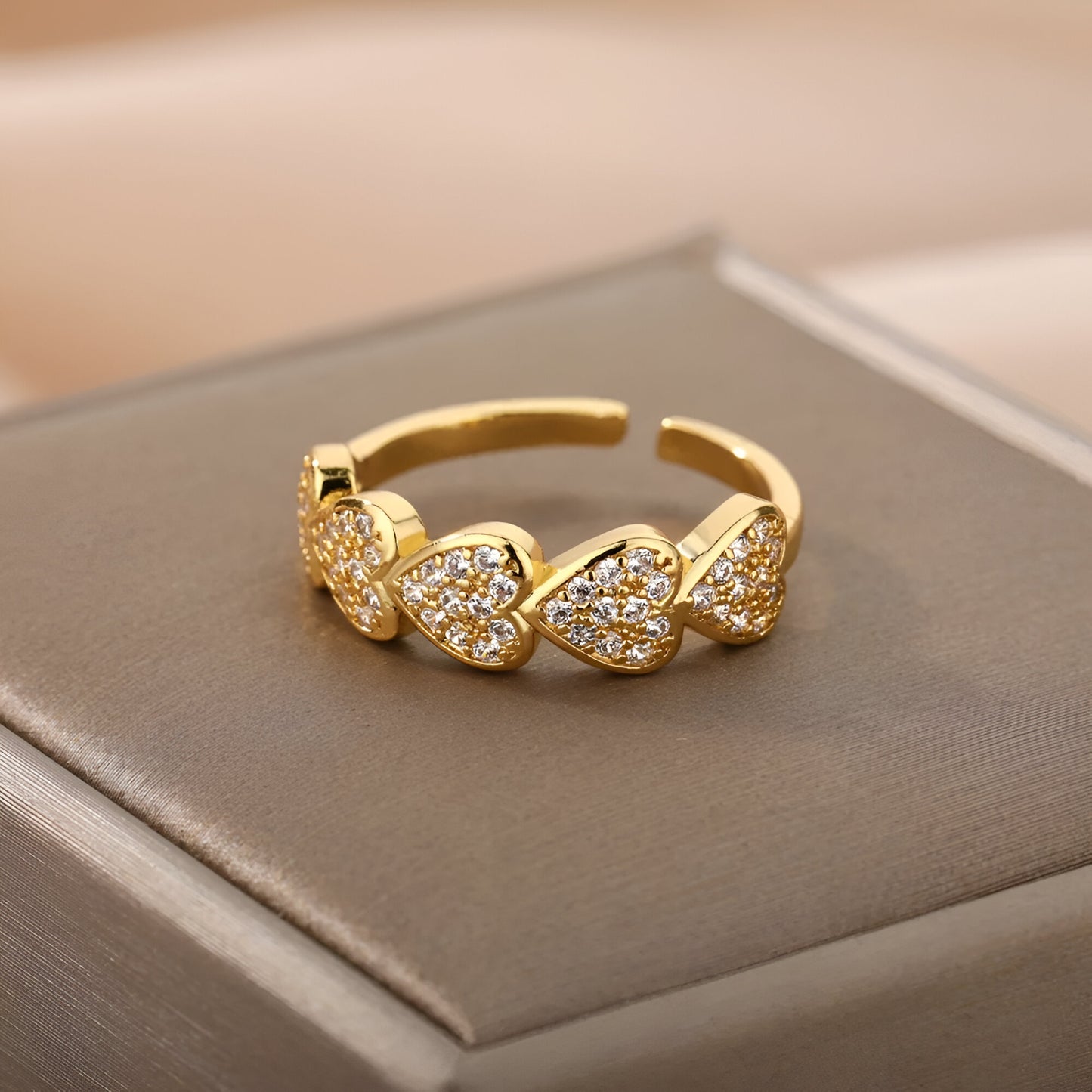Vue rapprochée de la bague ouverte en or posée sur écrin, éclats de zircon étincelants sur cœurs dorés