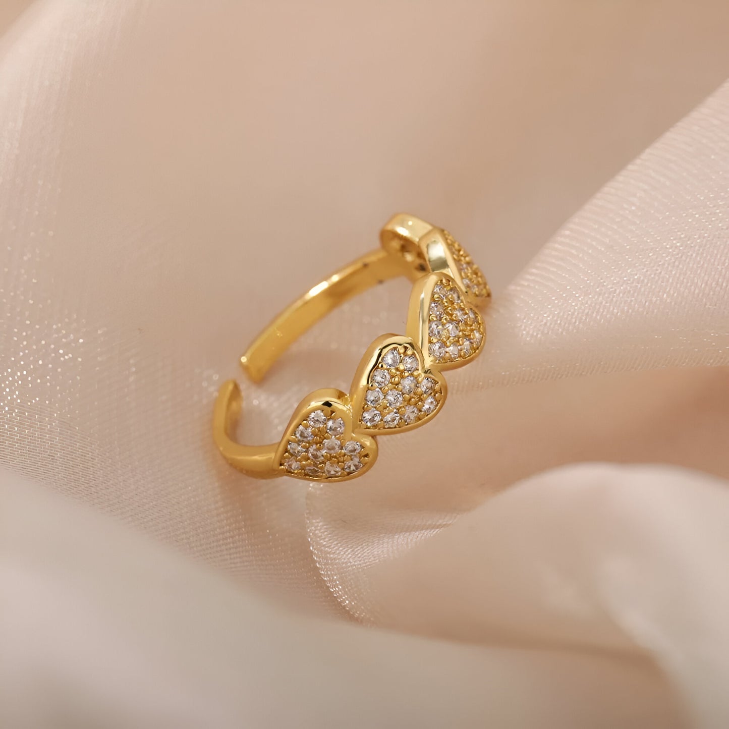 Bague ouverte en or scintillante sur tissu beige, ornée de cœurs en zircon pour un look romantique et luxueux