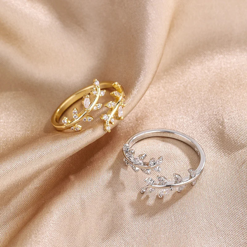 Variantes de la bague ouverte feuille de laurier Caméllia en argent 925 plaqué or jaune ou plaqué or blanc et diamants posées sur un drap.