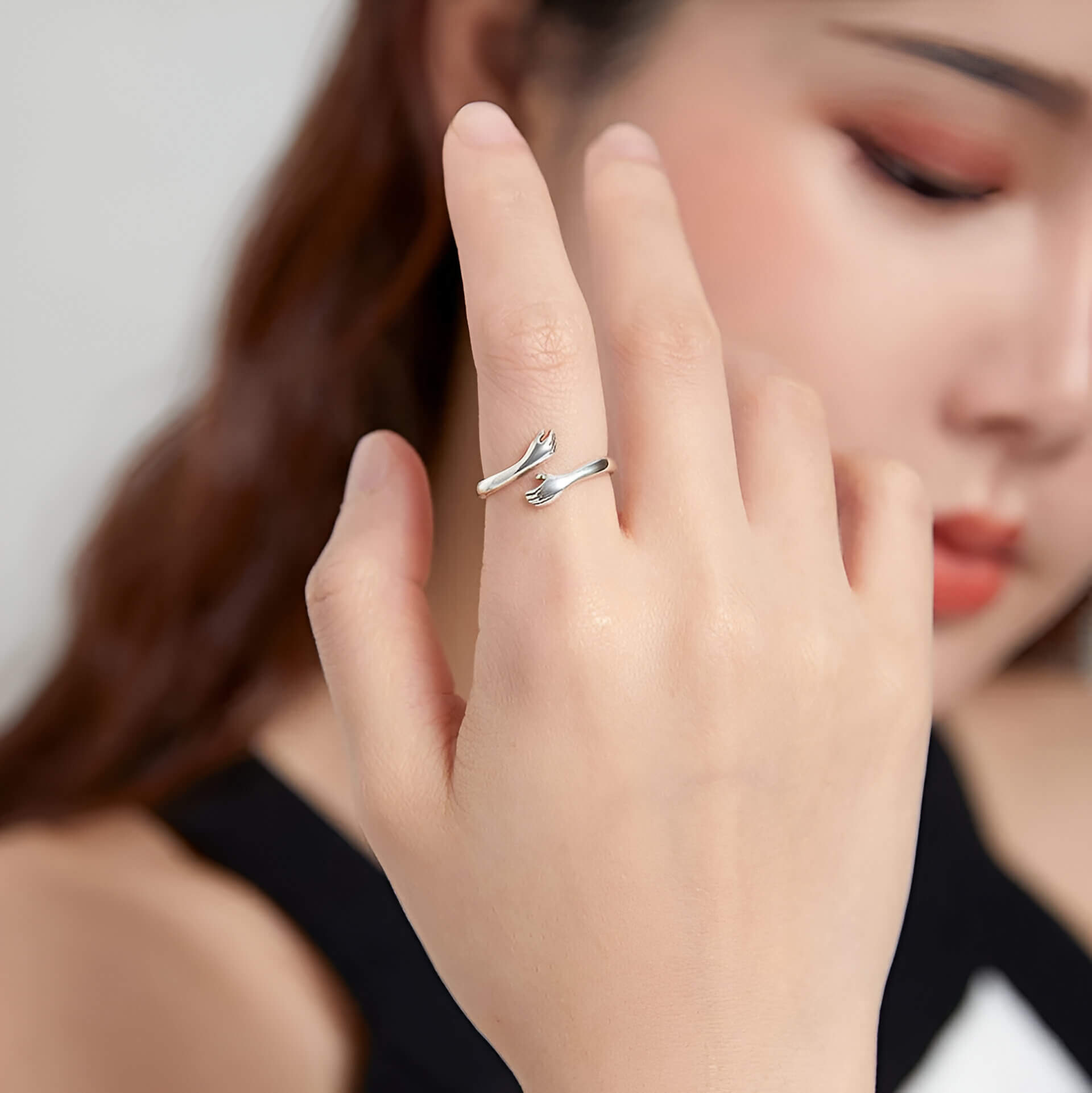 Bague ouverte main enlacée en argent sterling 925 plaqué or blanc portée au doigt d'une femme vue de face.