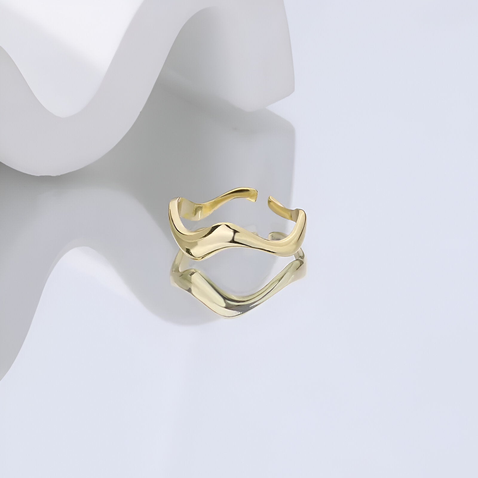 Bague ouverte ondulée Diana en argent 925 plaqué or jaune à plat sur une surface réfléchissante.