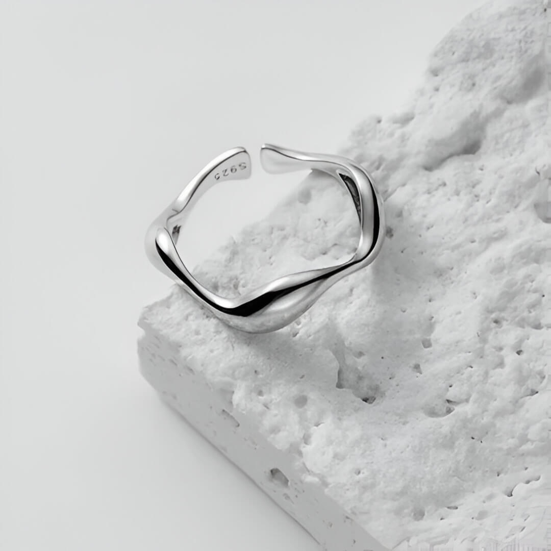 Bague ouverte ondulée en or blanc posée.