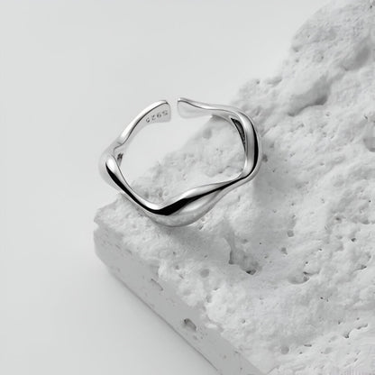 Bague ouverte ondulée en or blanc posée.