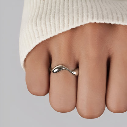 Bague ouverte ondulée en or blanc portée au doigt d'une femme vue rapprochée.