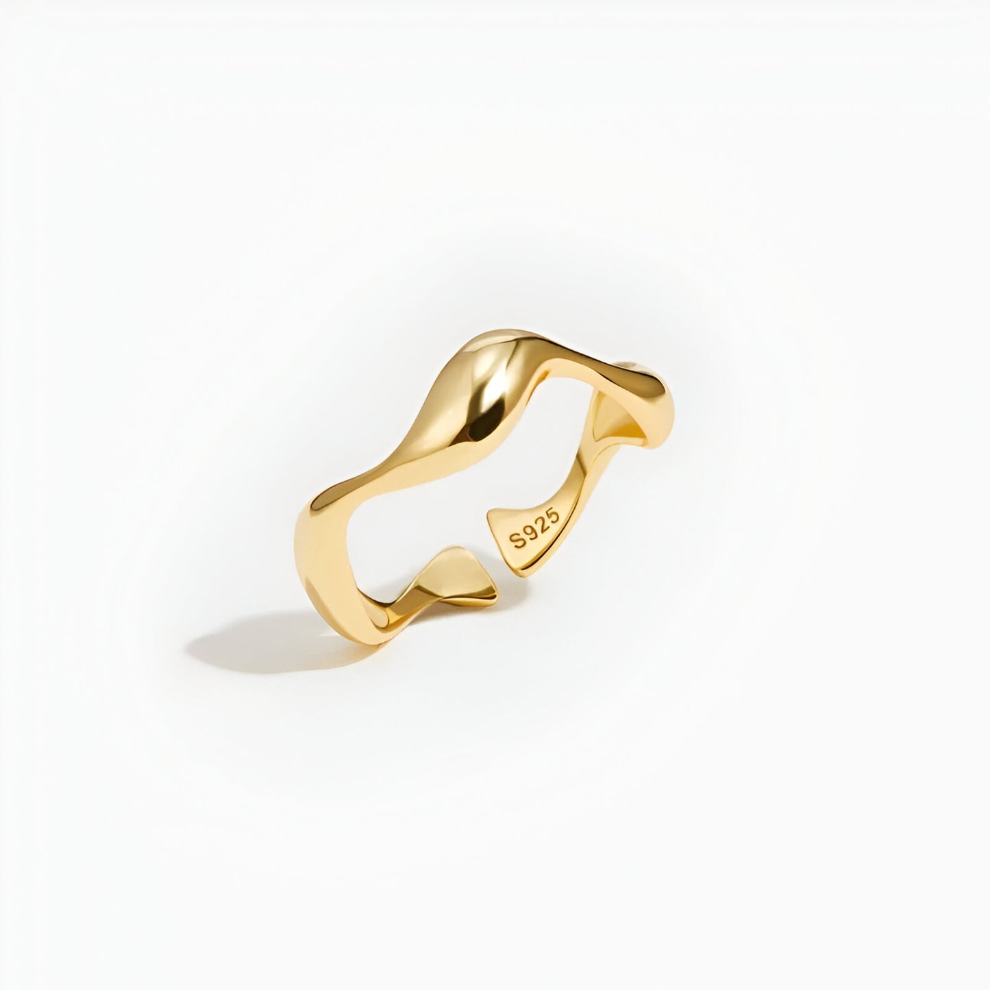 Bague ouverte ondulation en or debout sur un fond blanc.