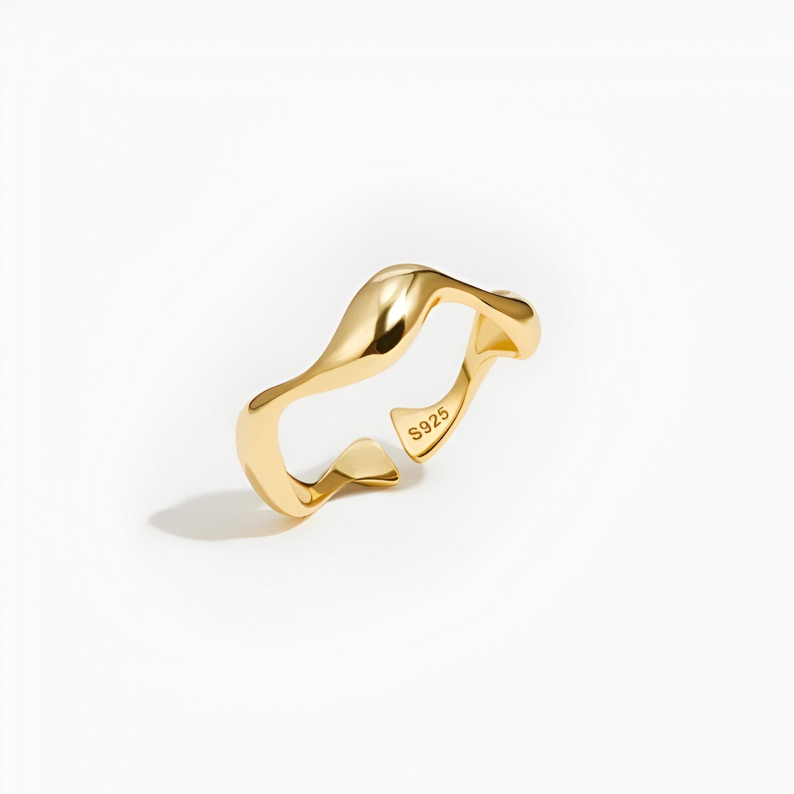 Bague ouverte ondulation en or debout sur un fond blanc.