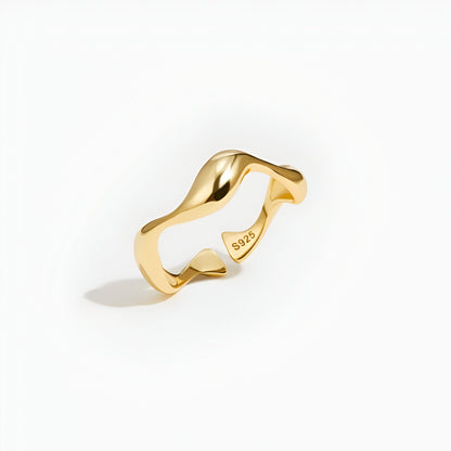 Bague ouverte ondulation en or debout sur un fond blanc.
