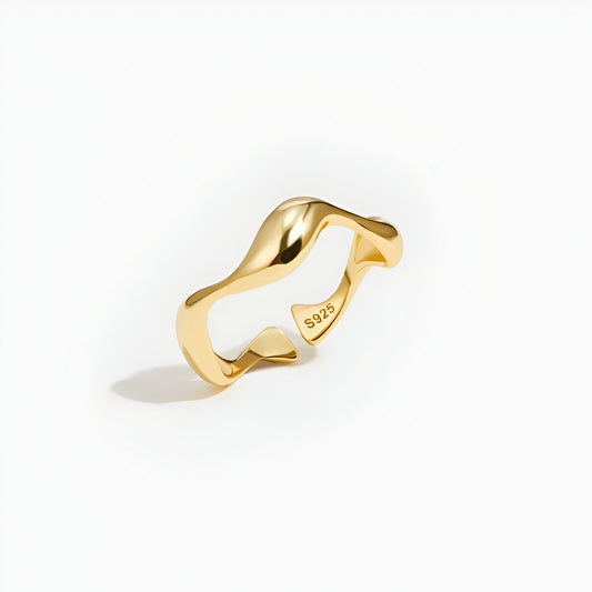 Bague ouverte ondulation en or debout sur un fond blanc.