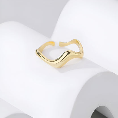 Bague ouverte ondulation en or à plat vue de face posée sur un socle blanc.