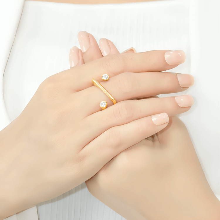 Bague fantaisie ouverte semi-tourbillon en acier inoxydable et or jaune sertie de cristaux portée au doigt d'une femme.