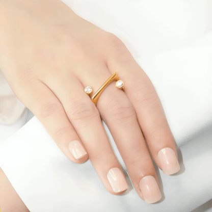 Bague fantaisie ouverte semi-tourbillon en acier inoxydable et or jaune sertie de cristaux portée au doigt d'une femme vue rapprochée.
