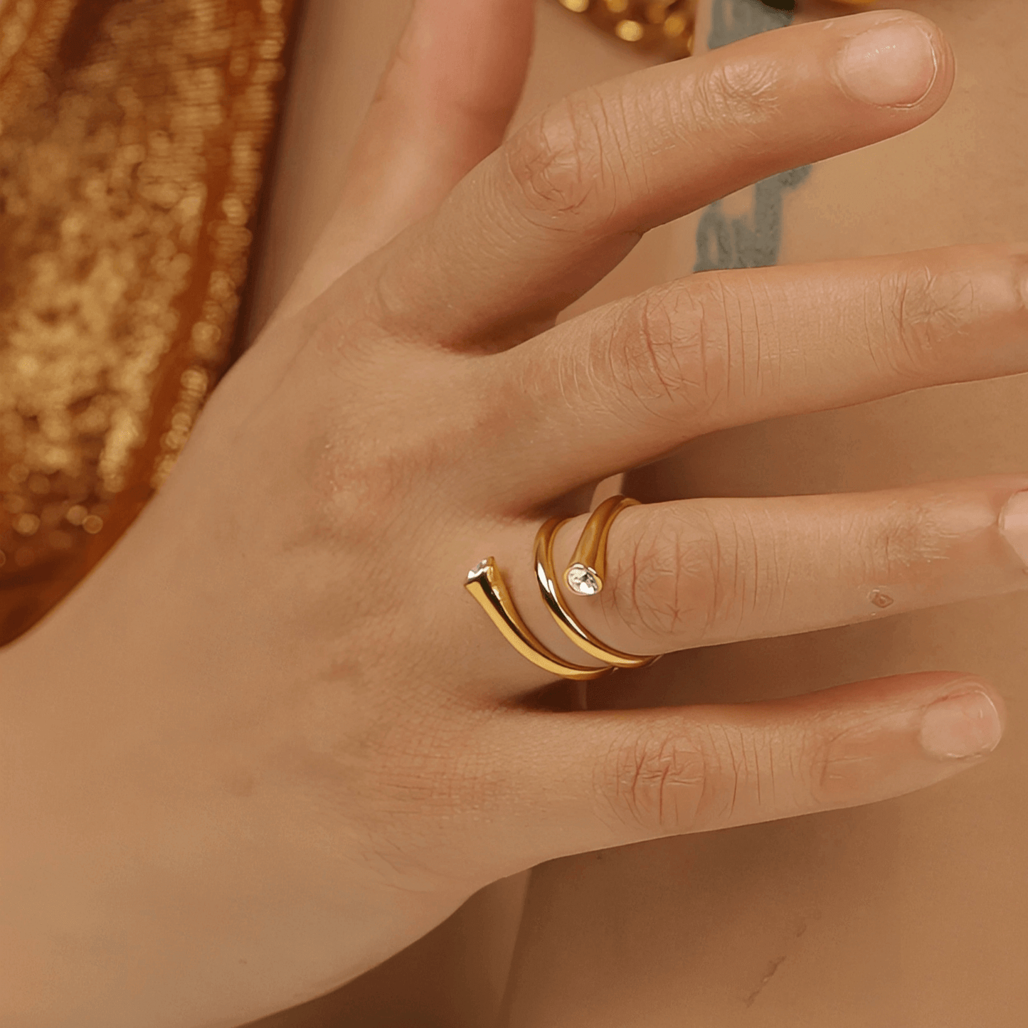 Bague fantaisie ouverte tourbillon en acier inoxydable et or jaune sertie de cristaux portée au doigt d'une femme vue rapprochée.