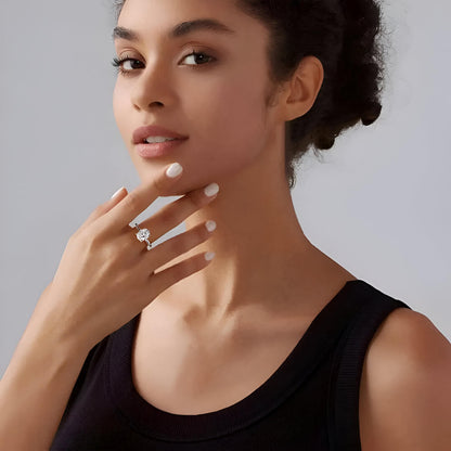 Bague solitaire en or blanc et diamant synthétique portée au doigt d'une femme brune.