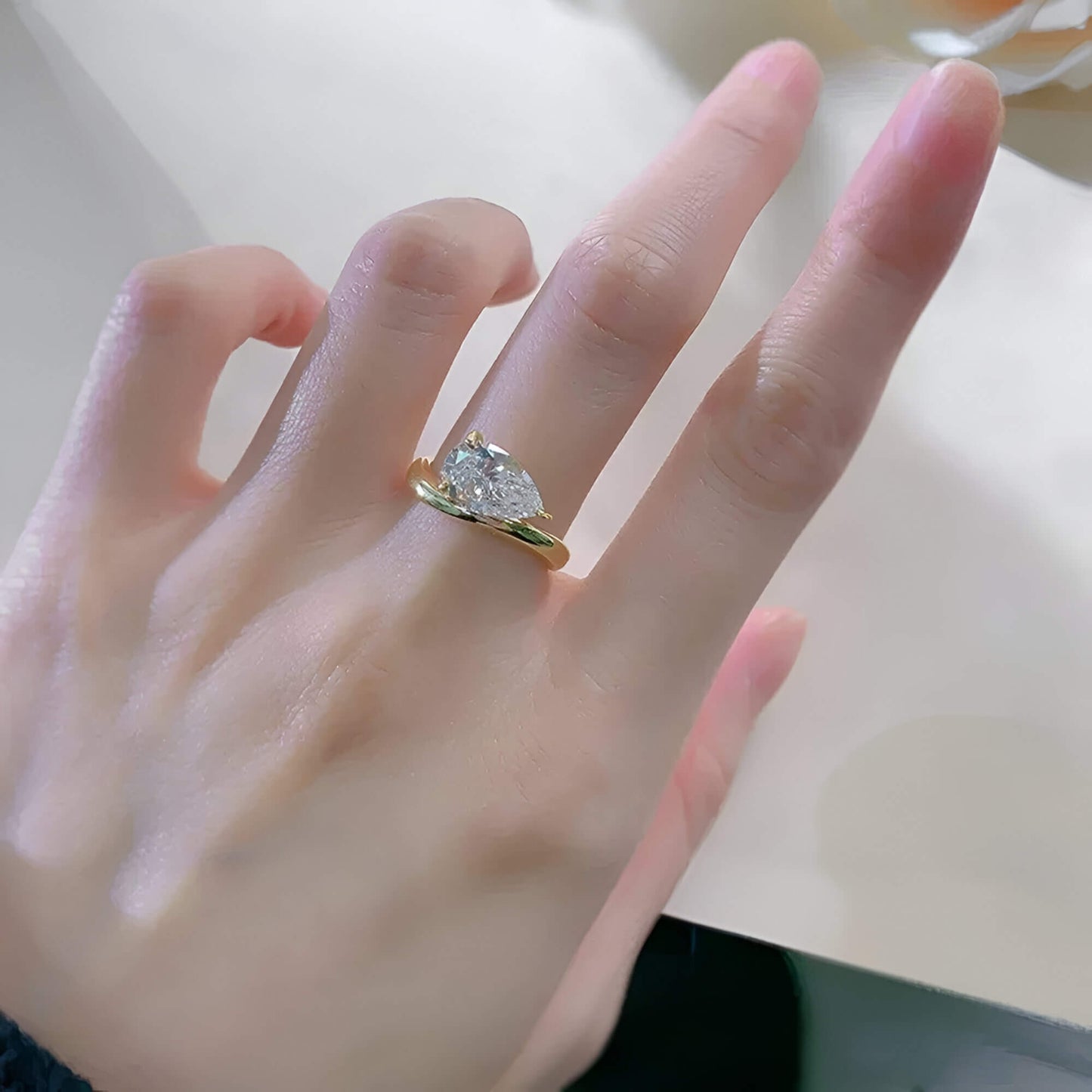 Bague solitaire courbée en or jaune et diamant synthétique portée au doigt d'une femme vue du dessus.