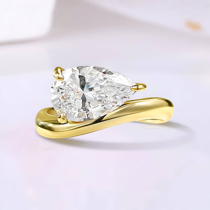 Bague solitaire courbée en or jaune et diamant synthétique sur fond uni.