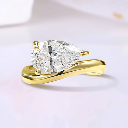 Bague solitaire courbée en or jaune et diamant synthétique sur fond uni.