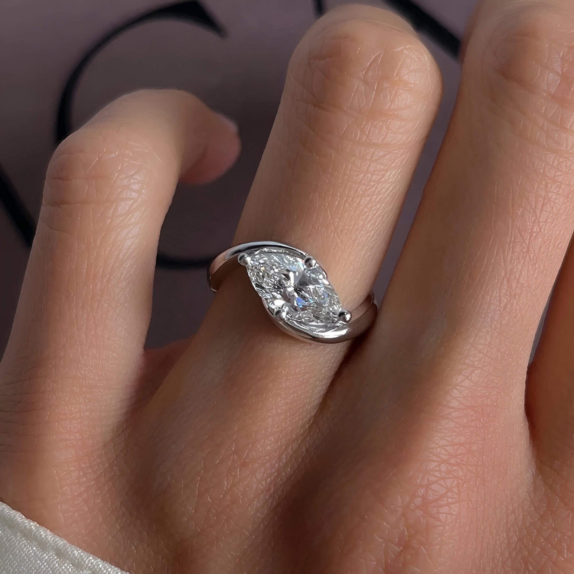 Bague solitaire courbée en or blanc et diamant synthétique portée au doigt d'une femme.