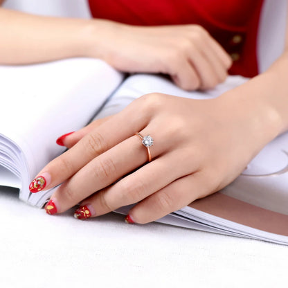 Bague solitaire en or rosé et oxyde de zirconium portée au doigt d'une femme vue de loin.