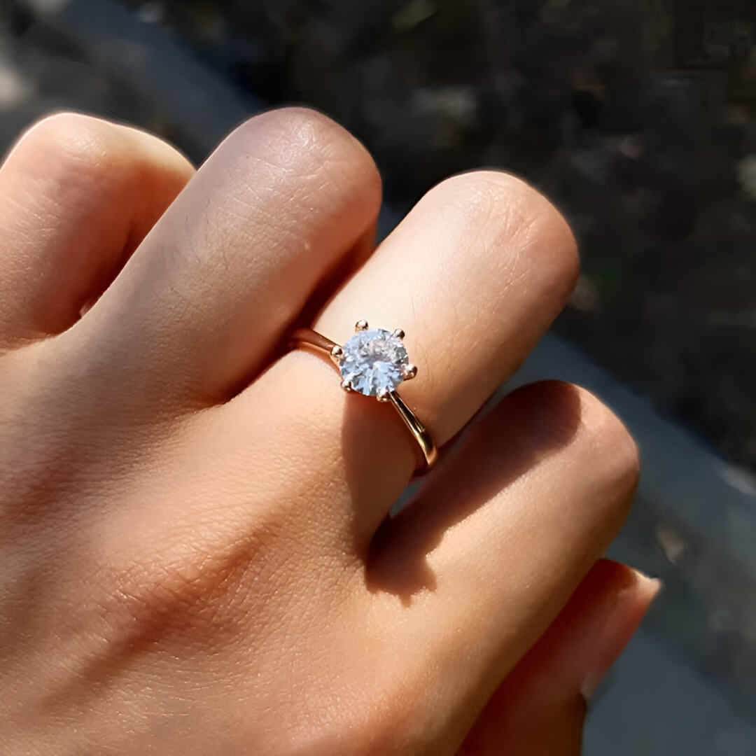 Bague solitaire en or rosé et oxyde de zirconium portée au doigt d'une femme.