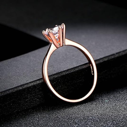 Bague solitaire en or rosé et oxyde de zirconium posée sur un rebord noir.