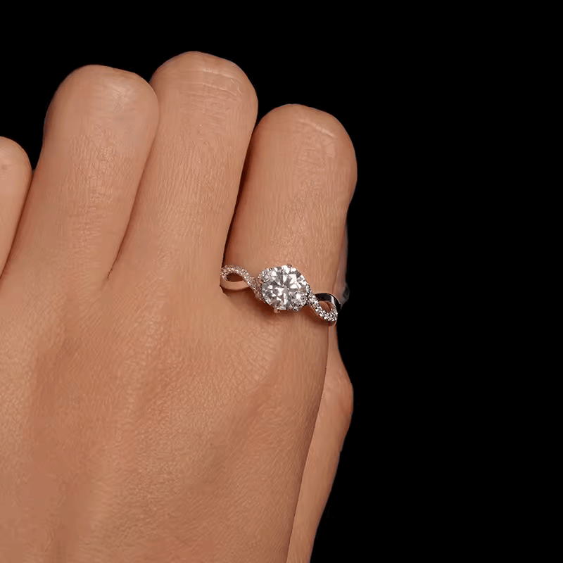 Bague solitaire courbée en or blanc et diamants synthétiques portée au doigt d'une femme vue du dessus.