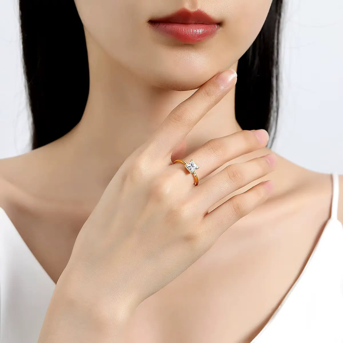 Bague solitaire princesse serti semi-clos en or jaune et diamant synthétique portée au doigt d'une femme.