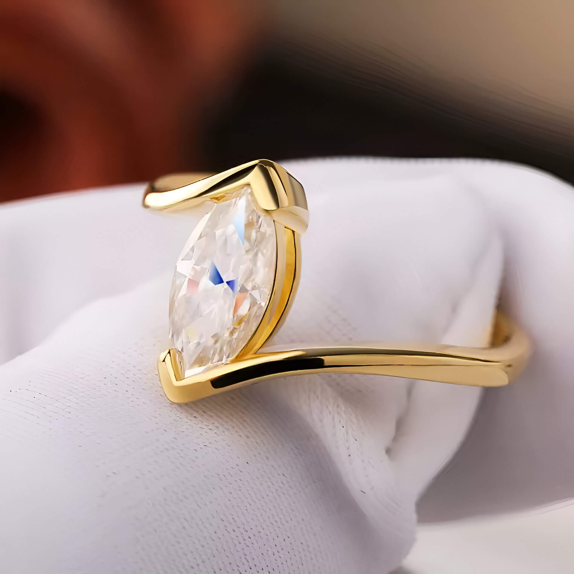 Bague solitaire serti barre Amina en argent 925 plaqué or jaune lumineux et diamant navette montrée entre les doigts d'une main gantée vue de côté.
