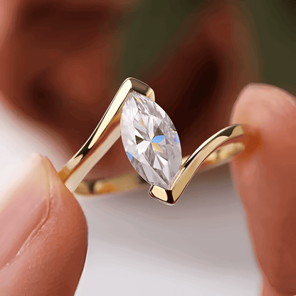 Bague solitaire serti barre Amina en argent sterling 925 plaqué or jaune et diamant navette montrée entre les doigts d'une femme vue de proche.