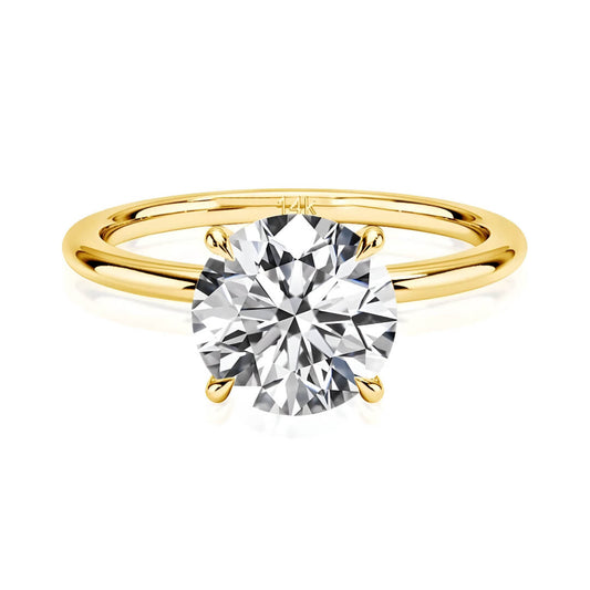 Bague solitaire quatre griffes en or jaune et diamant synthétique sur fond blanc.